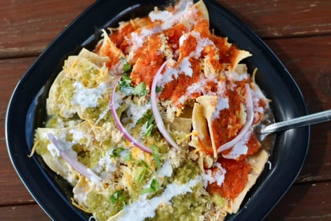 Black bowl of Asian noodles with red and green vegetables, topped with sliced onions and sesame seeds, with a spoon