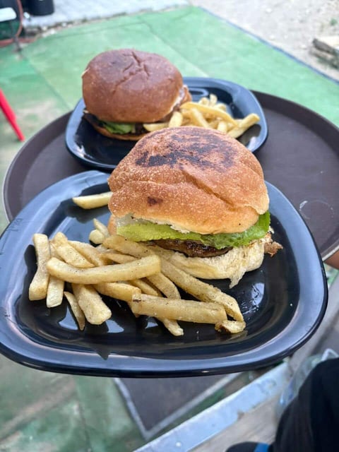 Two burgers with lettuce and sauce on buns, served with french fries on black plates outdoors
